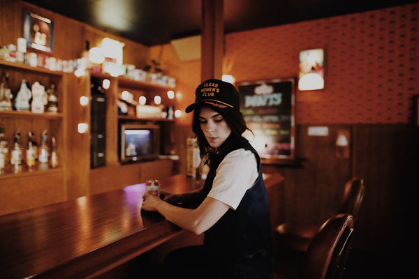 woman sitting at bar wearing a trucker hat